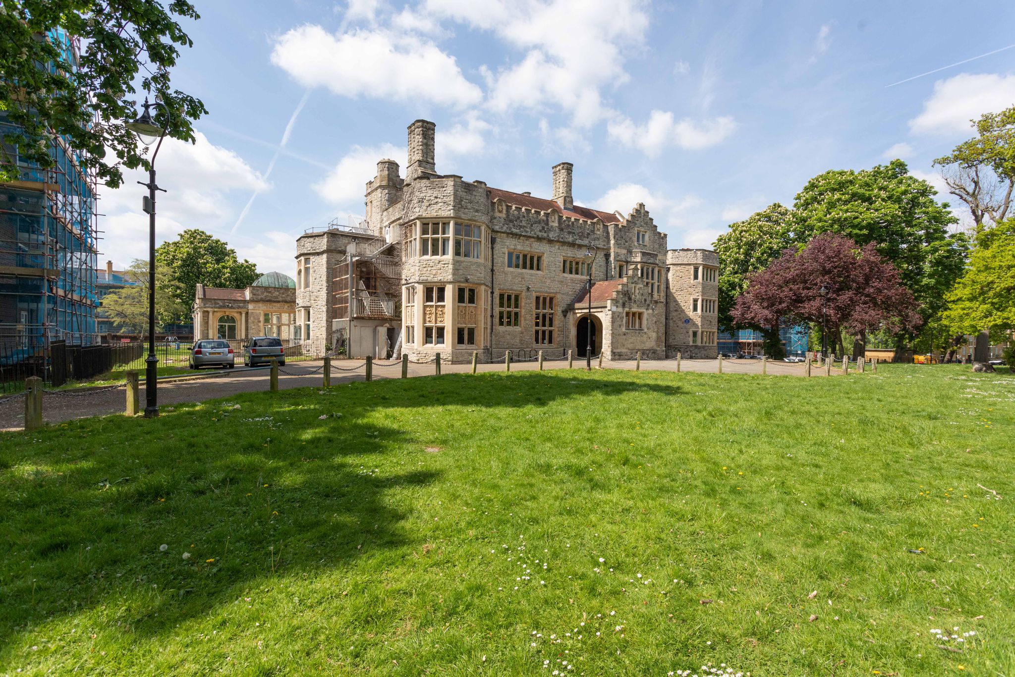 A large old manor house building with 2 stories and chimneys and turrets that make it look a bit like a castle, with a big green lawn out the front.